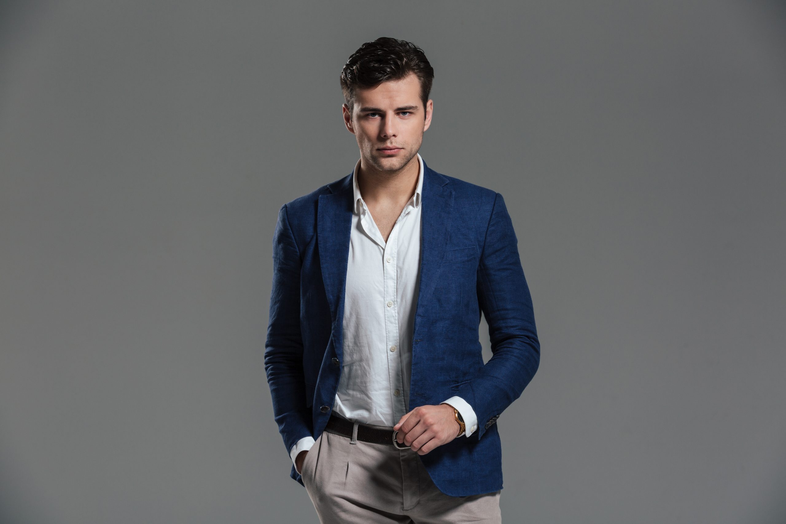 Portrait of a serious successful man dressed in a jacket standing and looking at camera isolated over gray background